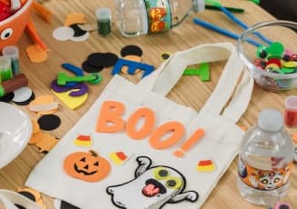 A table full of craft supplies and Pure Life purified water, building a Halloween-themed tote-bag.