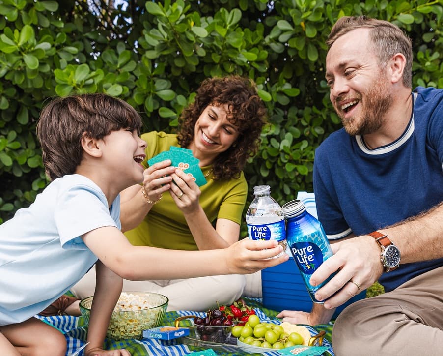 A family at a picnic outside enjoys games, food, and Pure Life purified water.