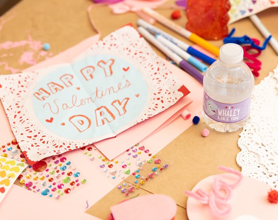 Materials and crafts of a Do-It-Yourself Valentine's Day card on a table with an 8 fluid ounce bottle of Pure Life purified water.