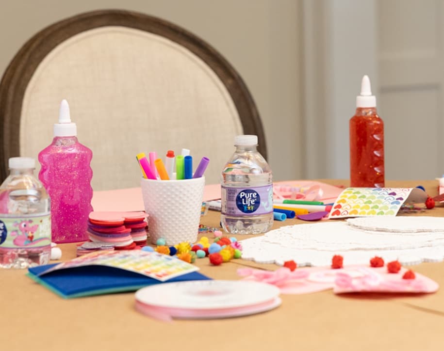 A table full of craft materials used to create Do It Yourself Valentine's Day cards, including Pure Life purified water.